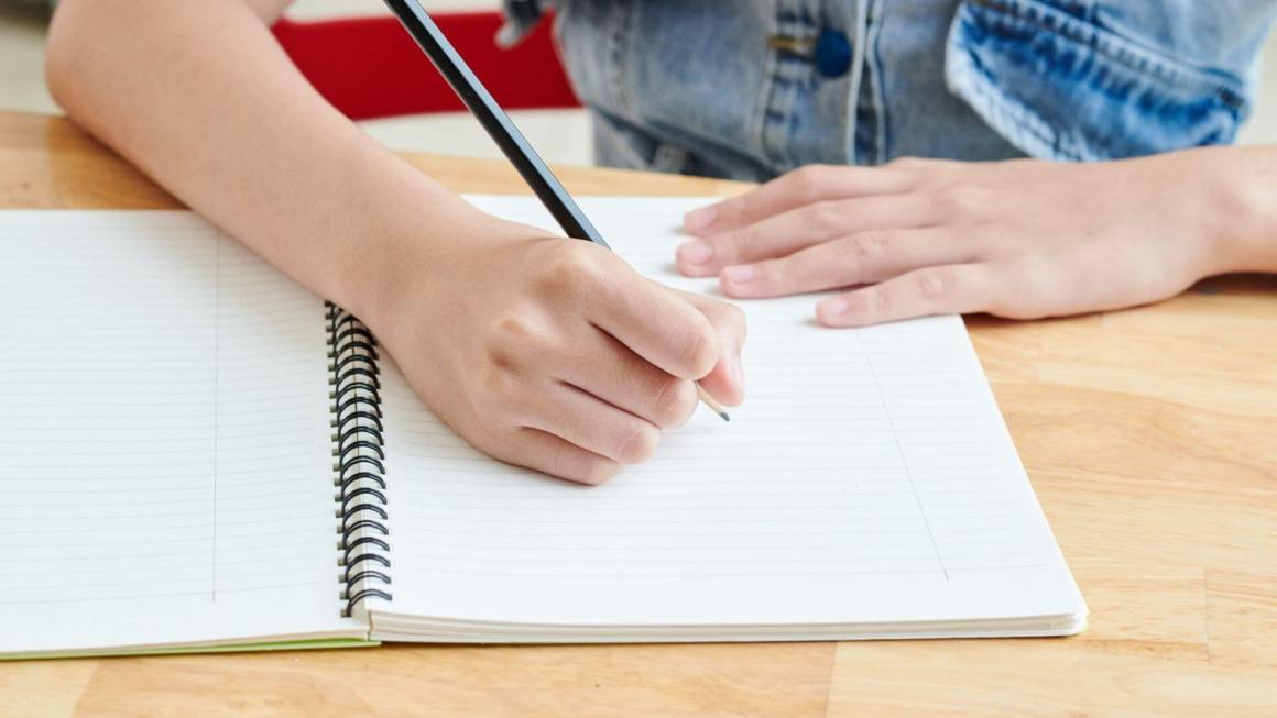 Person holding pencil to notebook, preparing to write an outline for an essay.