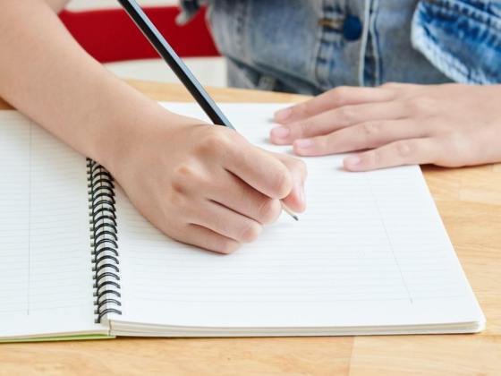 Person holding pencil to notebook, preparing to write an outline for an essay.