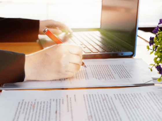 Woman with red pen marking up a research paper, next to a laptop