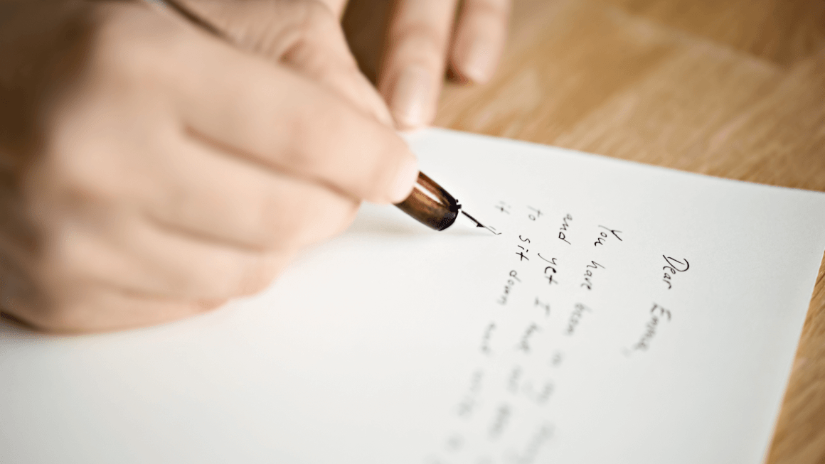 Close up of a person's hand writing a letter with an ink pen.