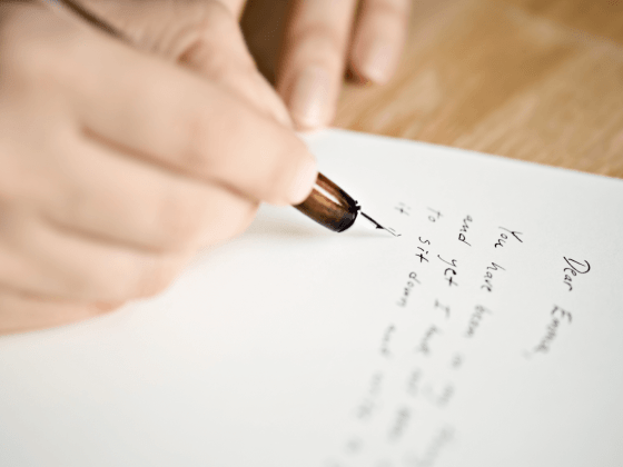 Close up of a person's hand writing a letter with an ink pen.