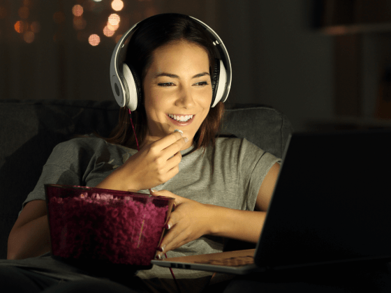 Woman wearing headphones and eating popcorn while watching a movie on her laptop.