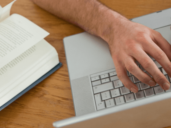 hands typing on a keyboard with an open book nearby.