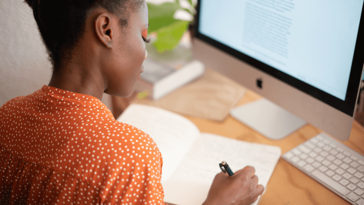 Woman writing in her notebook near computer