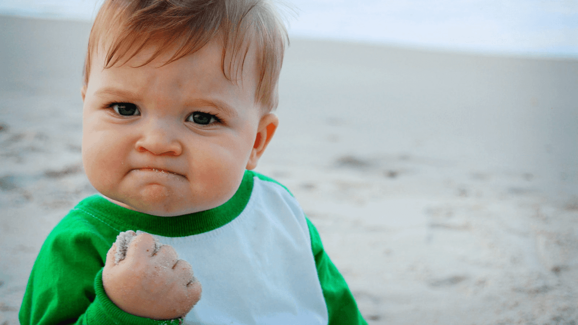 Success Kid meme, photo by Laney Griner; photo of a baby boy clutching a fistful of sand at the beach, looking very accomplished