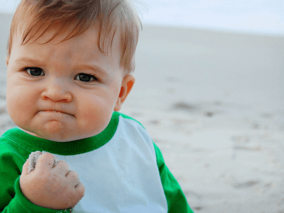 Success Kid meme, photo by Laney Griner; photo of a baby boy clutching a fistful of sand at the beach, looking very accomplished