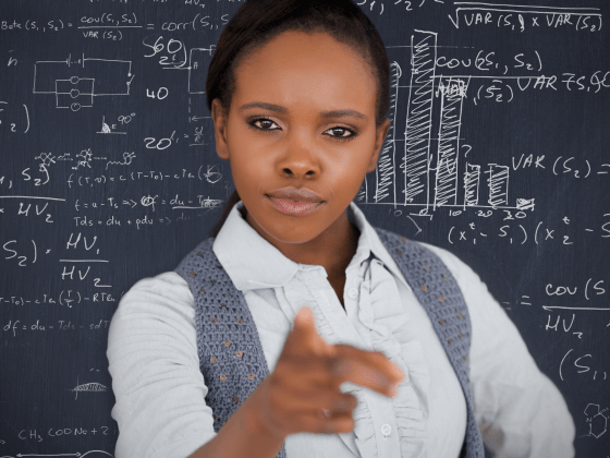 Teacher standing in front of a blackboard, pointing at the camera