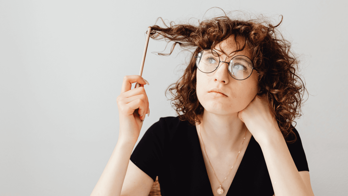 Woman looks thoughtfully at pencil while twirling it in her hair