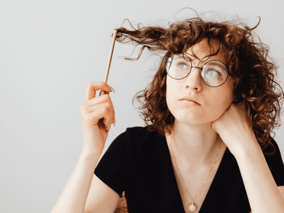 Woman looks thoughtfully at pencil while twirling it in her hair