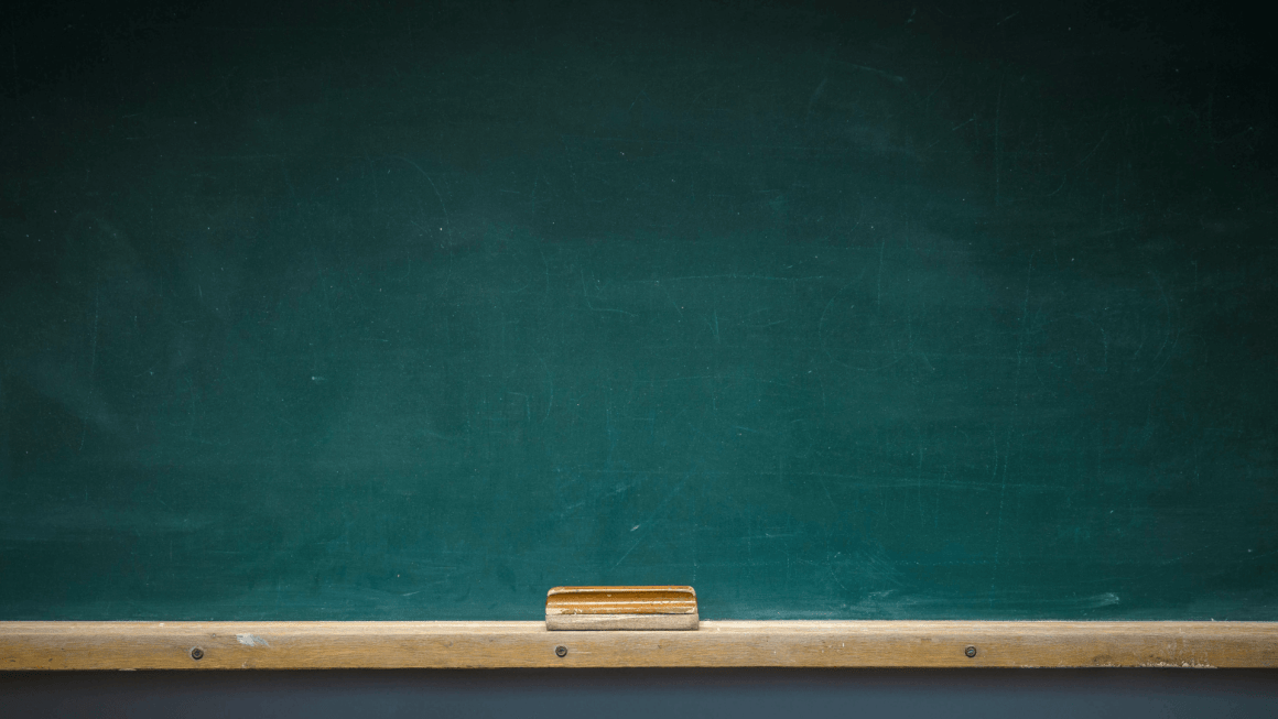 Empty green chalkboard with wooden shelf and eraser.