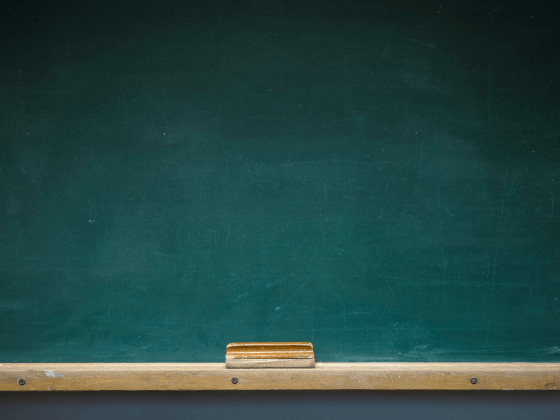 Empty green chalkboard with wooden shelf and eraser.